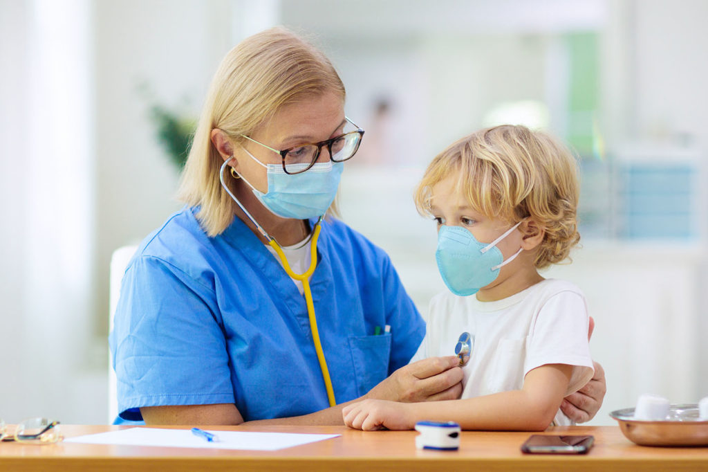 Pediatrician doctor examining sick child in face mask
