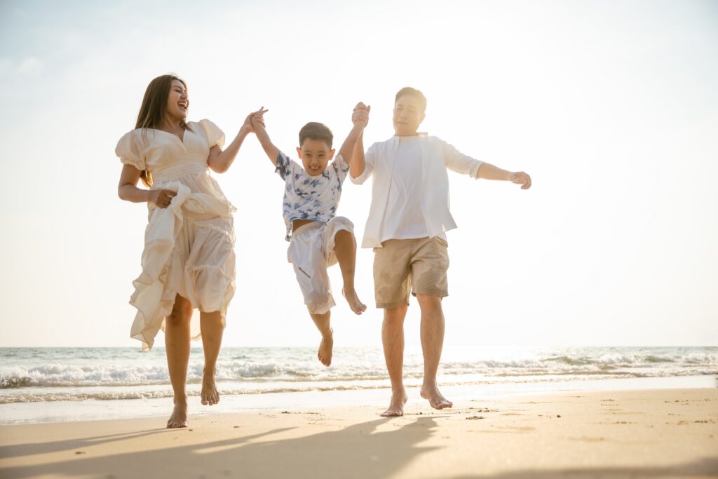 Happy family of 3 smiling as they walk along the beach
